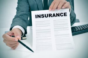 A young man in suit in his office showing an insurance policy and pointing with a pen where the policyholder must to sign