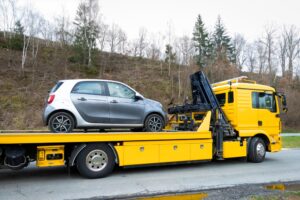 A breakdown service is loading a small electric car in a parking lot next to a country road after it stopped due to an empty battery. 