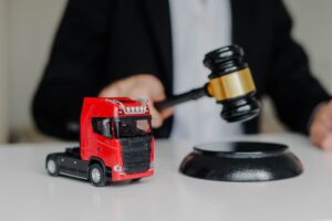 A male judge strikes a gavel on a block in a courtroom, symbolizing a prohibited export concept, with a toy tow truck placed on the table nearby.