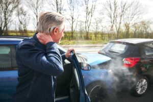 An elderly man with a whiplash injury exiting his car after a traffic accident. 