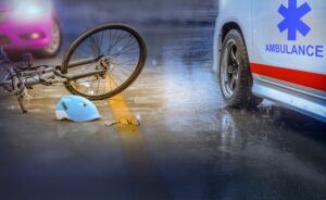 A car and a bicycle are involved in a collision on a wet road during rainy weather at night. The car shows visible damage, and the bicycle is knocked over, with its rider lying on the road, indicating the severity of the accident. The streetlights cast reflections on the wet pavement, and the scene conveys the dangerous consequences of drunk driving and road accidents during adverse weather conditions.