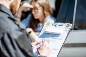 A close-up view of a policeman issuing a traffic fine to a young woman driver. The officer holds a folder with the fine documents in hand, while the woman, seated in her car, listens attentively. The focus is on the folder, which contains the citation for violating traffic rules. The scene conveys a moment of law enforcement in action, emphasizing the process of issuing a traffic ticket.