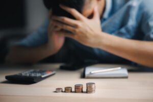 A distressed man sits with his head in his hands, visibly depressed and overwhelmed by financial loss. His office desk is cluttered with papers, bills, and empty coffee cups, symbolizing his struggle with business failure. The man appears to have experienced a significant financial crisis, reflecting the themes of bankruptcy and loss. The scene conveys the emotional toll of financial setbacks and the impact of a business crisis.