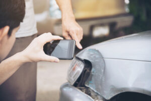 A person taking a photo of a damaged car with a smartphone, documenting evidence for an insurance claim or legal case.