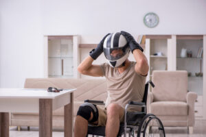 A man in a wheelchair wearing a motorcycle helmet and protective gloves, symbolizing recovery and the challenges faced after a motorcycle accident.