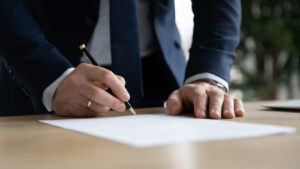 A professional in a suit signing a legal document on a desk, symbolizing legal paperwork or an attorney handling a case.