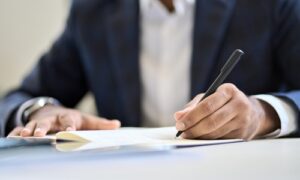 A person in a suit writing on a document with a pen, representing legal paperwork or signing an important agreement.