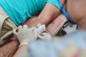 A medical professional wearing gloves applies a bandage to a person's arm, representing treatment for a dog bite or other injury.