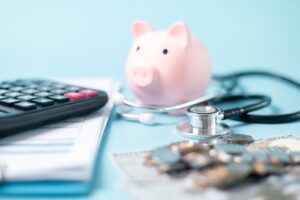 A piggy bank, stethoscope, calculator, and coins on a desk, symbolizing medical expenses, insurance claims, and financial planning.