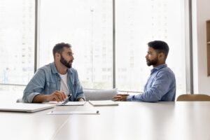 Two men sitting at a table in an office, engaged in a serious discussion, representing a legal consultation or insurance claim discussion.